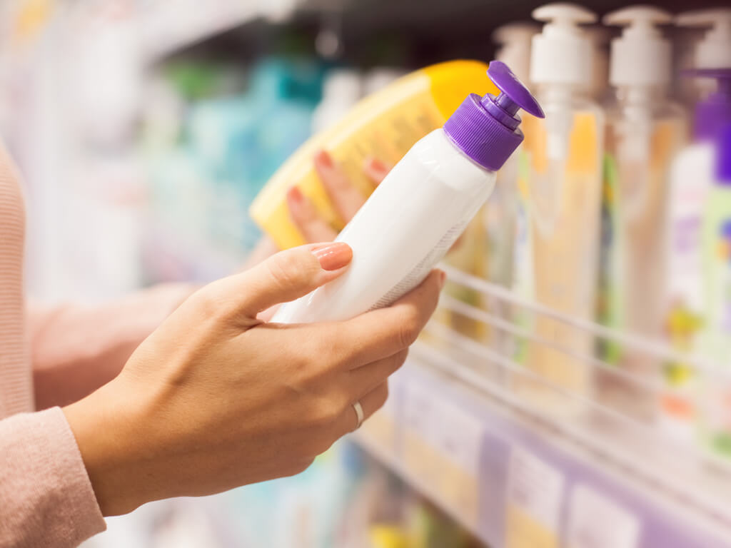 A woman looking at a bottle of sunscreen at the store.