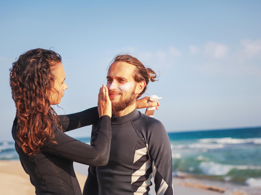 A couple applying sunscreen at the beach to prevent sunburns.