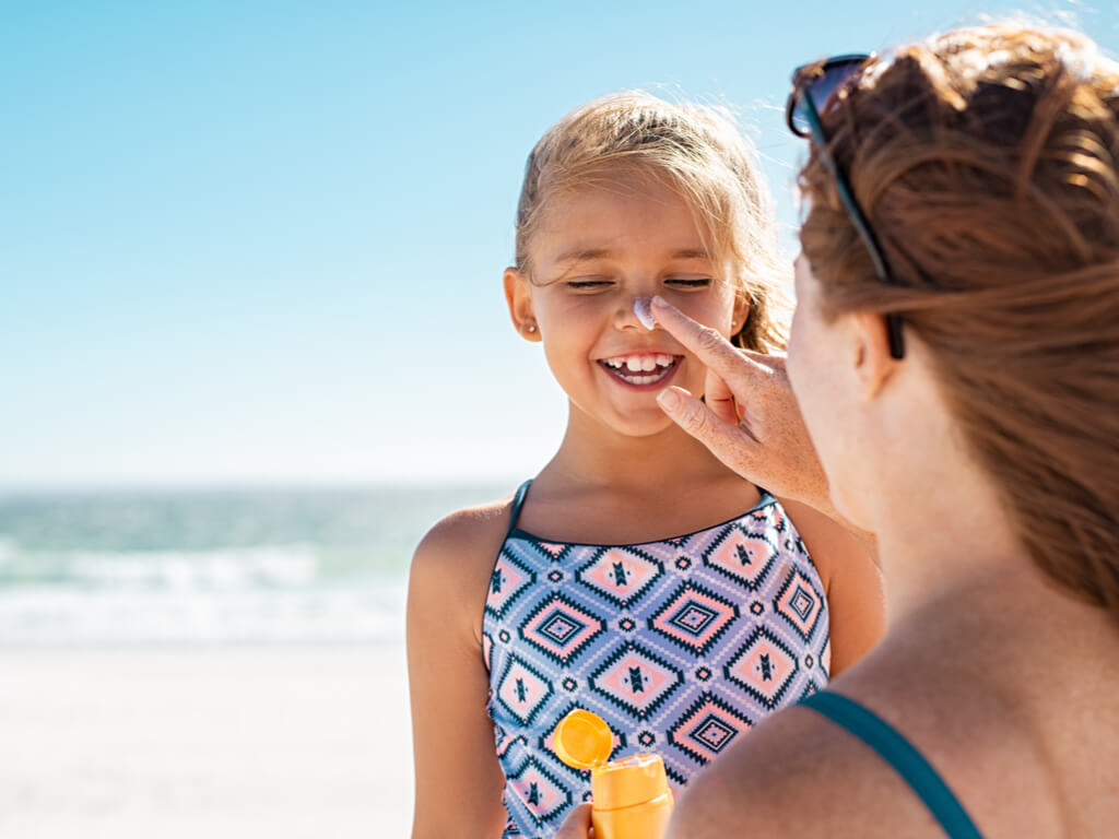 A mother putting sunscreen on her child's nose while at the beach.